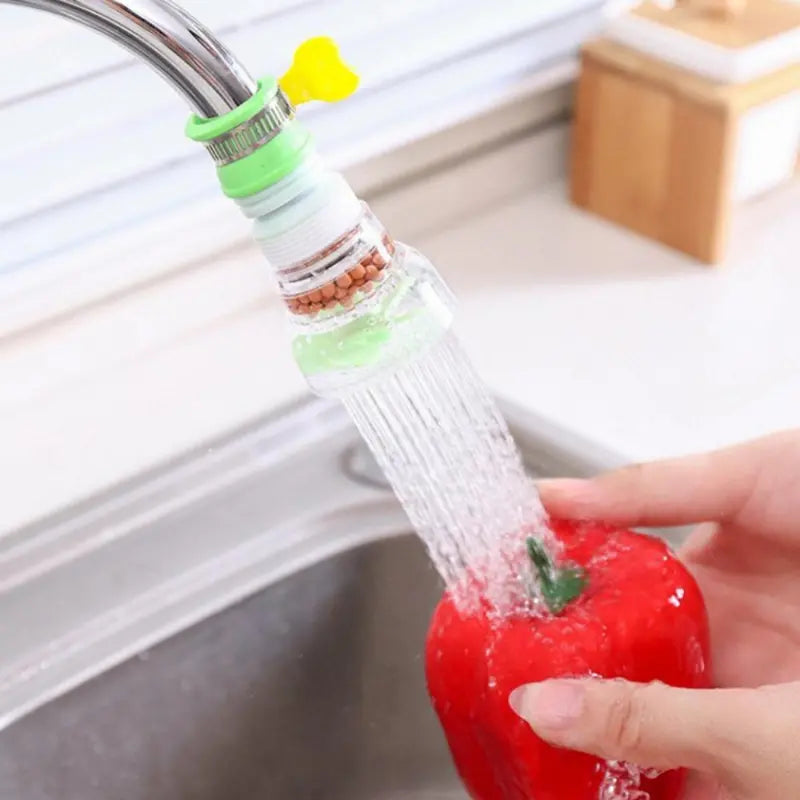 Red bell pepper being rinsed under water from a kitchen faucet with a filter attachment.