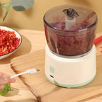 Small food processor with ground meat on a wooden surface, surrounded by ingredients.