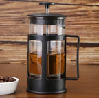 French press with coffee and a bowl of coffee beans on a wooden surface