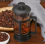 French press filled with coffee next to a bowl of coffee beans on a wooden surface
