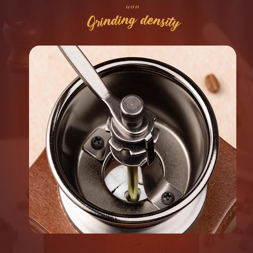 Close-up of a manual coffee grinder with a spoon inside, on a wooden surface.