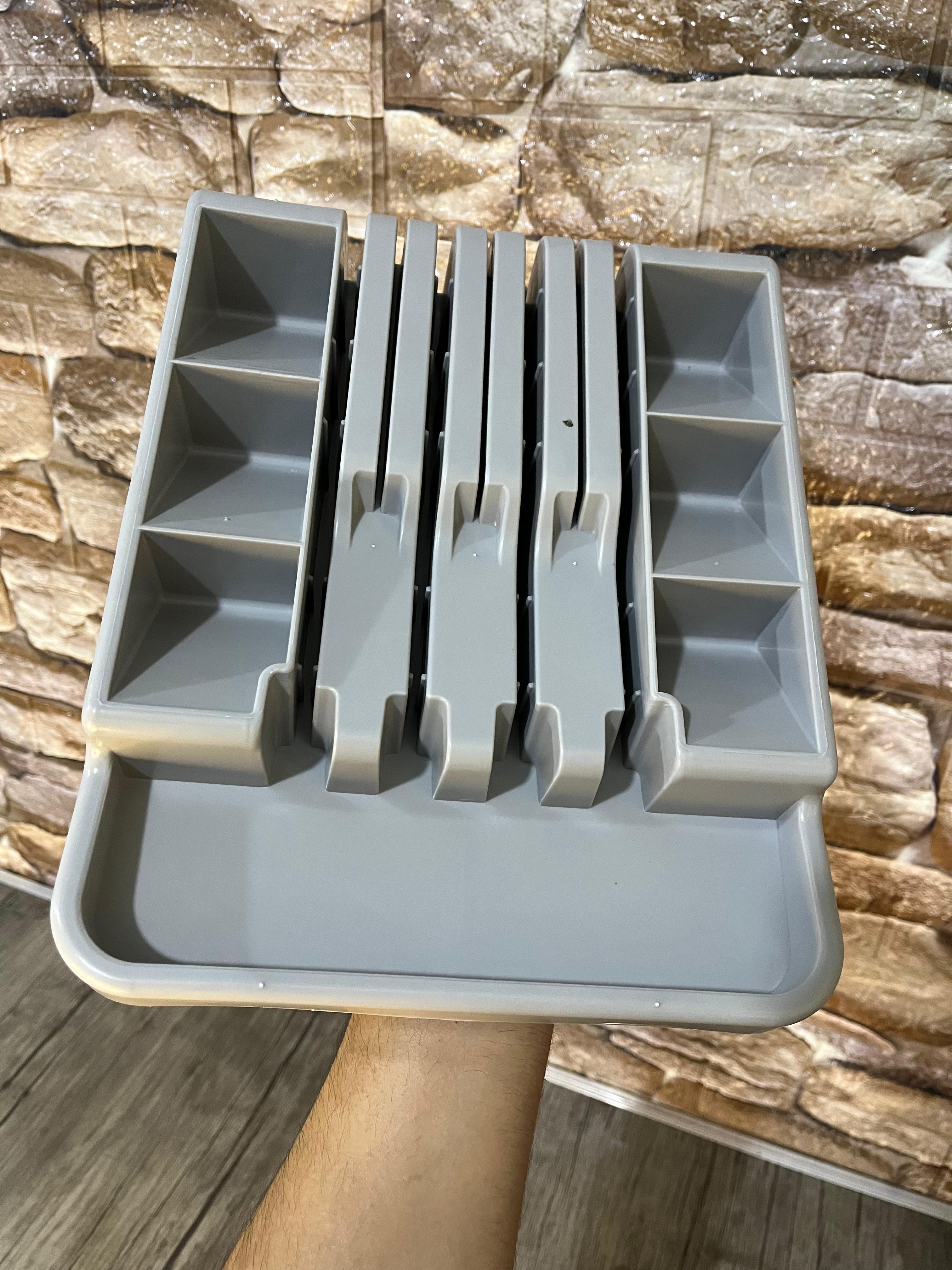 Gray knife sharpener with multiple slots against a stone wall background