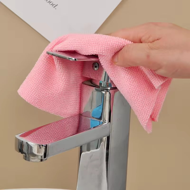 Person cleaning a faucet with a pink cloth against a beige background