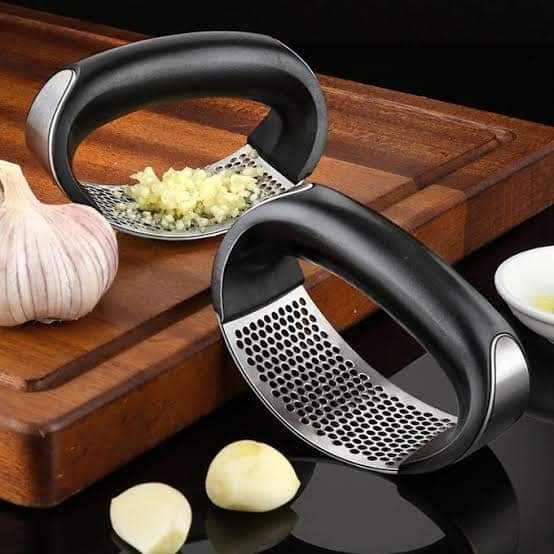 Garlic press on a wooden cutting board with garlic cloves and minced garlic.