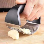 Garlic press being used to crush garlic on a wooden surface