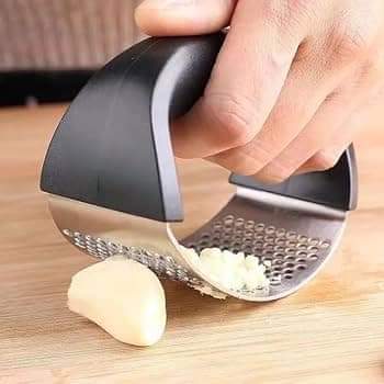 Garlic press being used to crush garlic on a wooden surface
