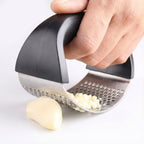 Hand using a garlic press to crush garlic on a white background