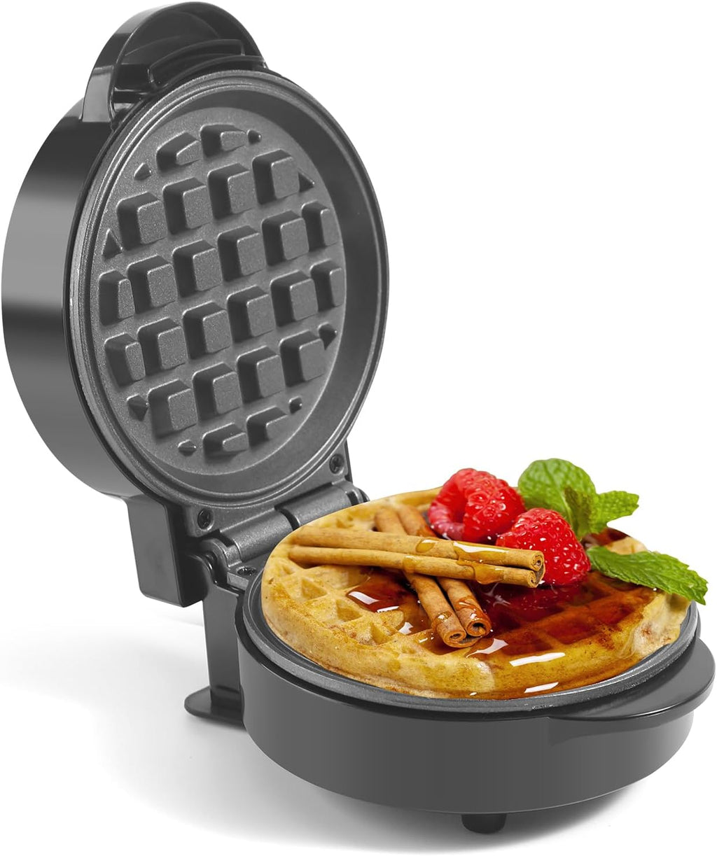Waffle maker with a cooked waffle inside, topped with berries and cinnamon sticks on a white background