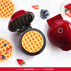 Red waffle maker with a cooked waffle inside, surrounded by berries on a white background.