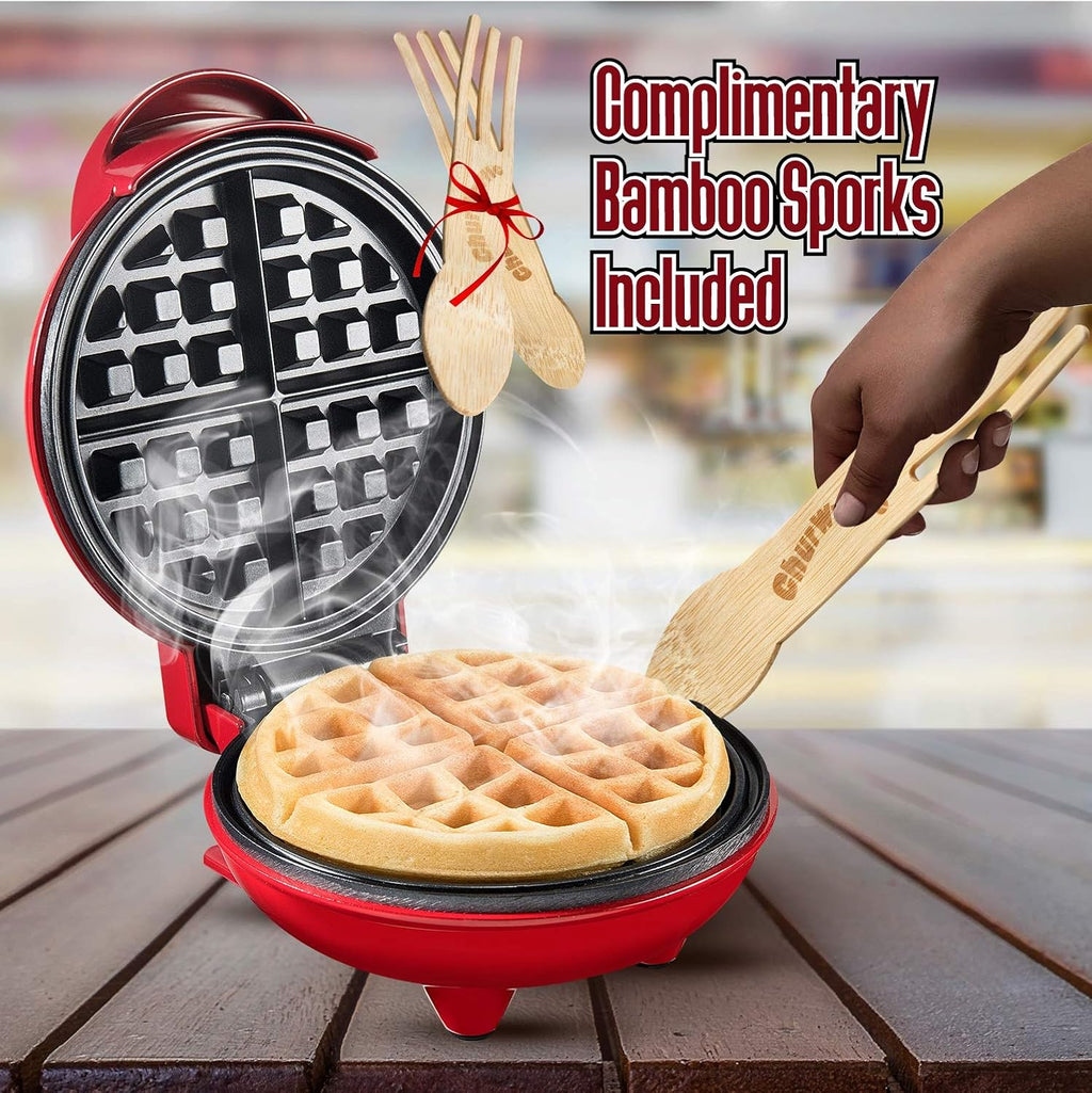 Red waffle maker with a waffle inside, accompanied by bamboo sporks on a blurred background.