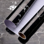 Roll of black marble patterned vinyl wrap on a dark marble surface