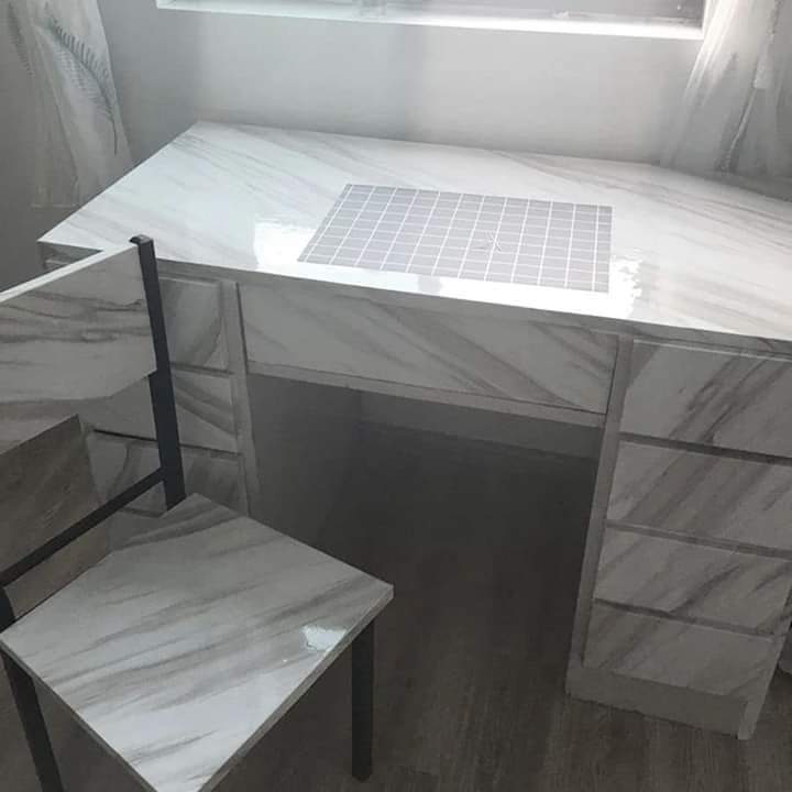 White marble-style desk with a chair in a room with sheer curtains.
