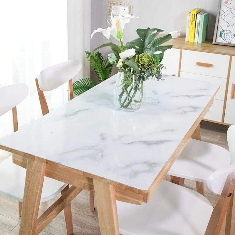 Dining table with marble-like surface and wooden legs, surrounded by chairs in a bright room.